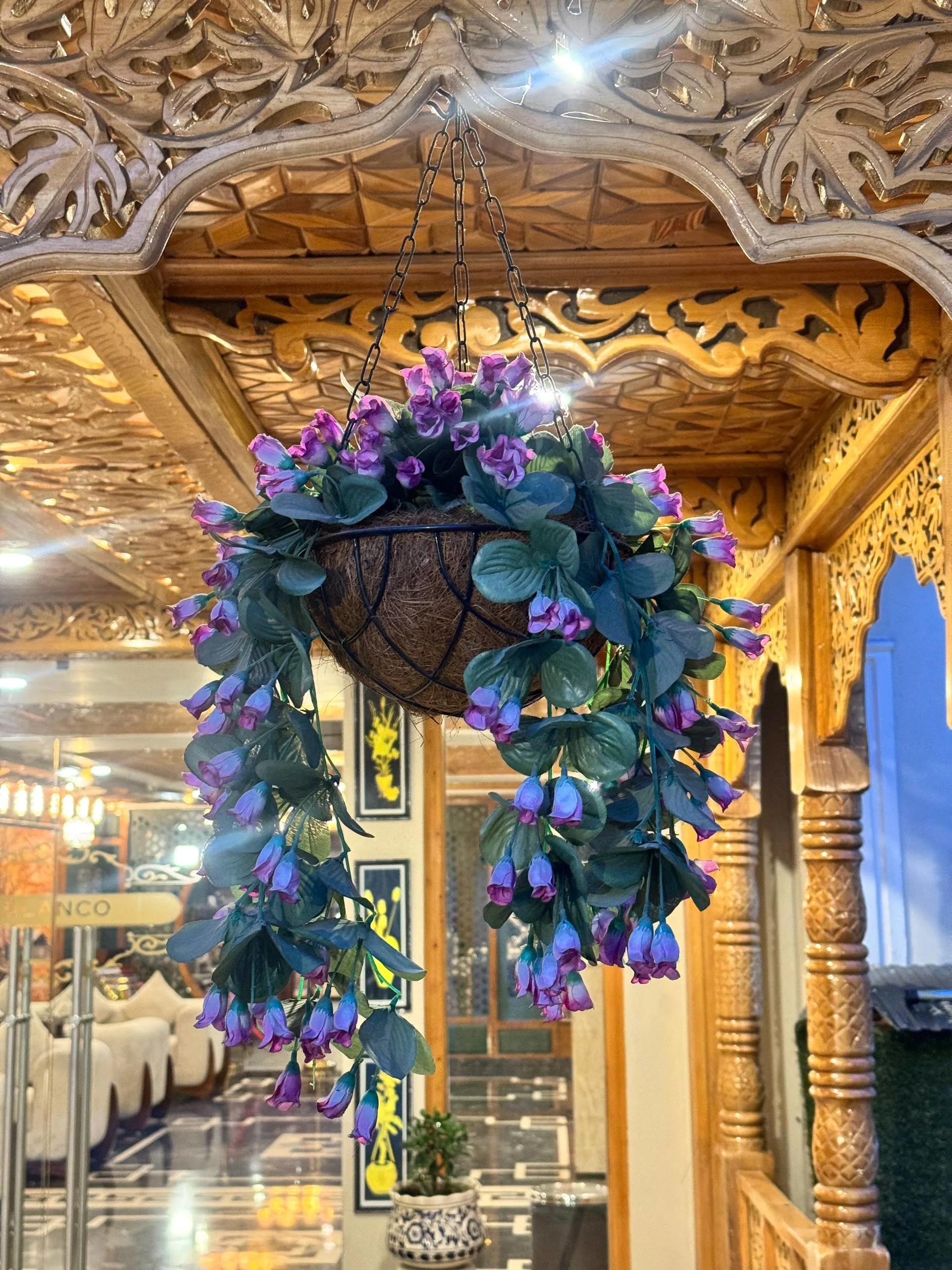 A hanging basket of flowers beneath carved walnut-wood arches at Blanco Hotel